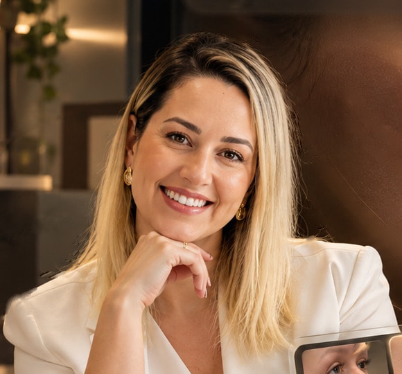 Dra. Thayse Pereira sorrindo, de blazer branco, em seu consultório